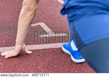 Fast Runner In Blue Sneakers Is Ready To Run On Track Number One. An Athlete Starting From The First