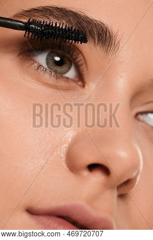Closeup Young Female With Gray Eyes Applying Mascara On Eyelashes With Spoolie Brush And Looking Awa