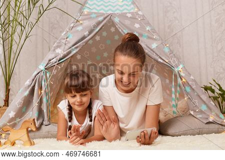 Indoor Shot Of Smiling Dark Haired Woman Lying With With Her Daughter On Floor Near Peetee Tent With