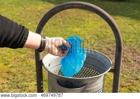 Close-up Of Man Throwing Away Trash In Garbage Container While Taking A Walk In Park