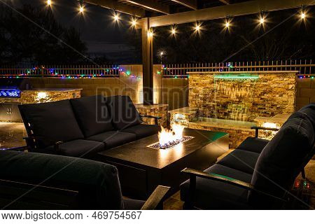 A Resort Style Backyard At Night With A Waterfall, Pergola, And A Firepit