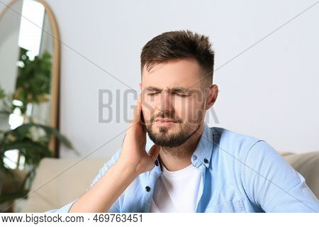 Young Man Suffering From Ear Pain At Home. Space For Text