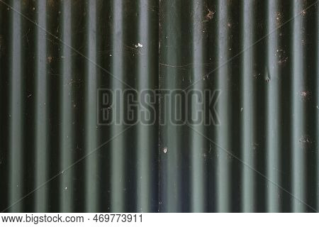 Two Scrappy Looking Sheets Of Dark Green Corrugated Iron Roofing With Holes And Cobwebs, Parallel To