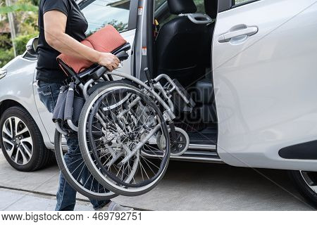 Asian Woman Folding And Lift Up Wheelchair Into Her Car. Accessibility Concept.