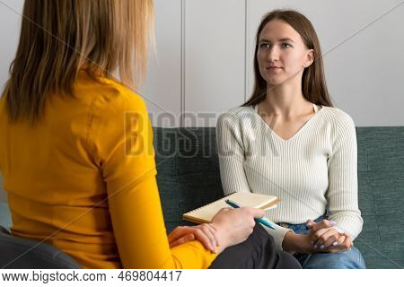 Young Woman Attentively Listens To A Psychologist At The Reception, Sitting On The Couch In The Offi