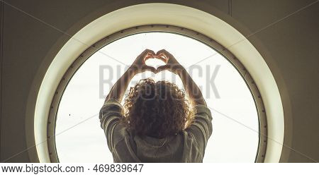 Back View Of A Woman Doing Heart Sign Gesture With Hands In A Circle Window Background And Light Out