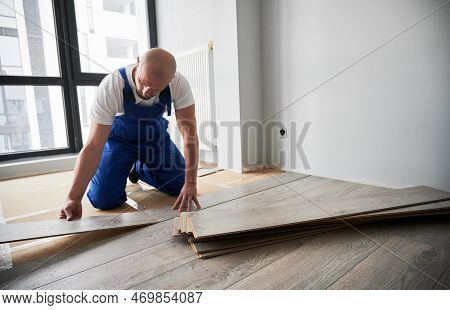 Man In Work Overalls Installing Laminate Wood Flooring In New Flat. Male Construction Worker Laying 