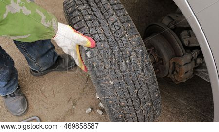 Mounting A Wheel With Studded Winter Tires On The Axle Of The Car, The Hands Of A Man In Gloves Put 