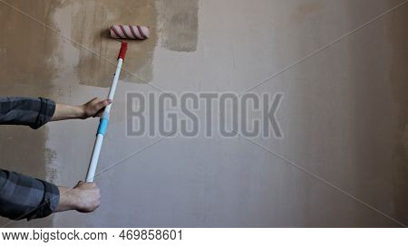 Applying Glue Or Primer To The Plastered Surface Of A Home Wall Using A Striped Roller On A Long Hom