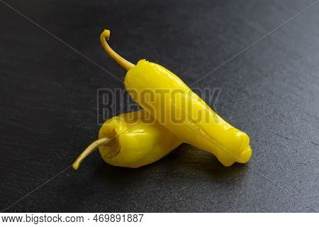 Two Pickled Yellow Peppers, Pepperoncini Or Friggitelli On Black Slate Background. Hot Pepper Marina