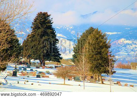 Vintage Headstones Surrounded By Trees On A Snow Covered Lawn During Winter With The Rocky Mountains
