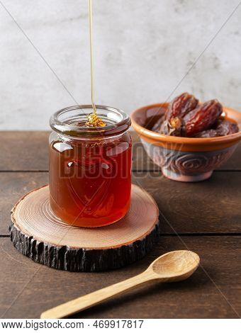 Natural Organic Healthy Date Syrup Flows Into A Glass Jar With Whole Dates And Wood Spoon On The Bac