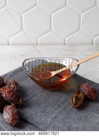Natural Organic Healthy Date Syrup In A Glass Bowl With Wood Spoon And Whole Dates On The Background