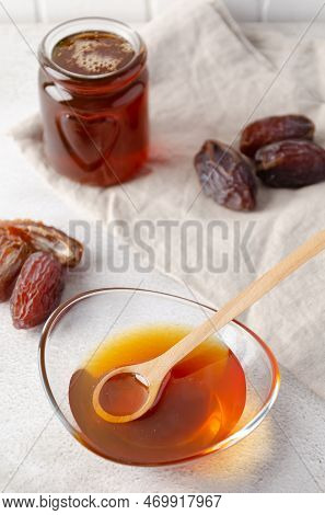 Natural Organic Healthy Date Syrup In A Glass Bowl With Wood Spoon And Whole Dates On The Background