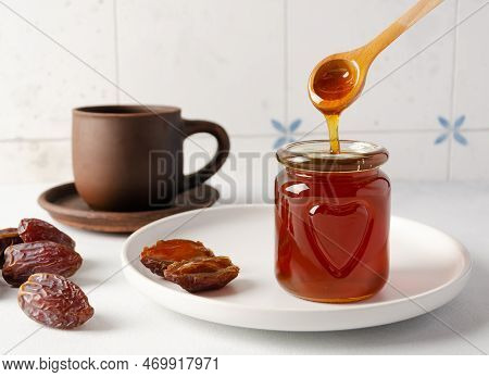 Natural Organic Healthy Date Syrup Flows From Wood Spoon Into A Glass Jar With Whole Dates And A Cap