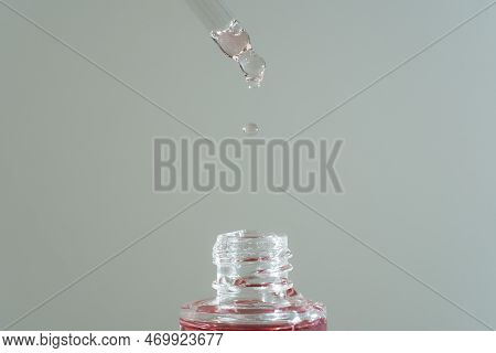 Pink Face Oil Drop From Glass Pipette Dropper. Macro Close Up For Cosmetic Neutral Background Bakuch