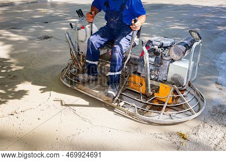 Worker Sitting On A Self-leveling Power Trowel Machine With Gas Engine Has Wheels With Pads, Plate A
