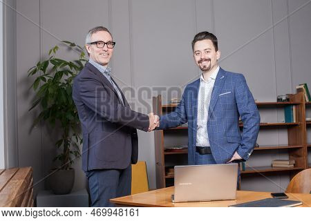 Two Happy Cherrful Businessman In Suit Making Handshake In Office, Business Succes Concept