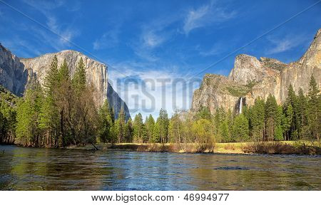 Yosemite Valley panorama showing the El Capitan, the Cathedral Rocks and the Bridalveil Falls,  with the Merced river in the foreground and blue sky with wispy clouds in the background.