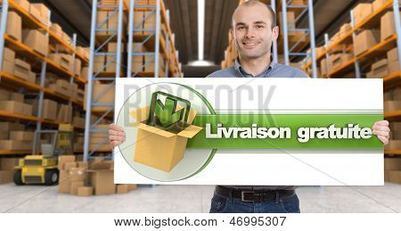  Un uomo che tiene un Livraison gratuite board, significato consegna gratuita in francese, in una distribuzione wareh