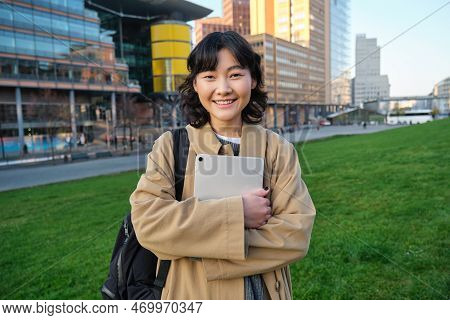 Happy Asian Girl Stands On Street, University Student Walks With Digital Tablet In Hands And Smiles,