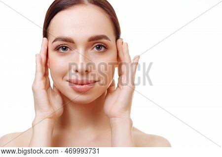 Young Brunette Woman With Flawless Skin And Bare Shoulders On A White Background Holds Her Hands Nea