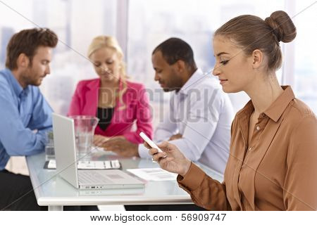 Young businesswoman sitting at a meeting, using mobilephone.