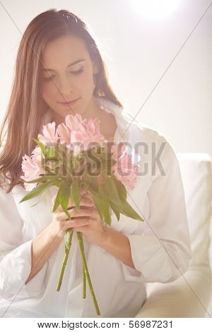 Portrait of lovely lady looking at bunch of pink lilies in her hands