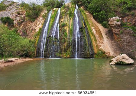 Three-jet scenic waterfall in the mountains. Three parallel streams of water running down the steep slope and fall in oval pool