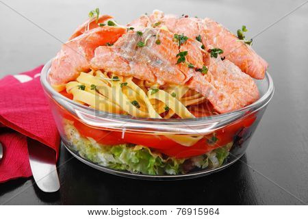 fresh fried natural pink salmon on italian traditional tagliatelle backed with tomato and vegetables served over black wooden table