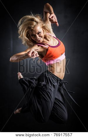 Young woman jumps while making aerobics exercises on gray background
