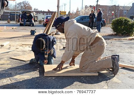 FERGUSON, MO/USA - NOVEMBER 25, 2014: A child and man work to assemble boards for windows of business in the aftermath of vandalism after grand jury decision not to indict Ferguson police Wilson.