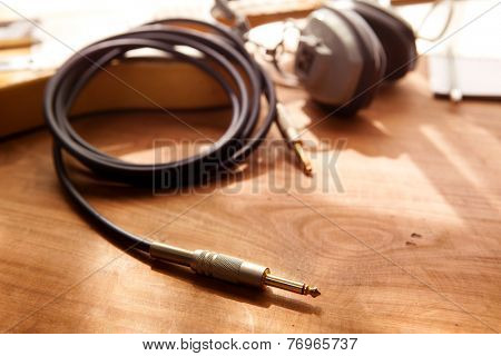Guitar recording. An electric guitar, and a professional use headphones on a rustic or bare wooden table, by the window. 