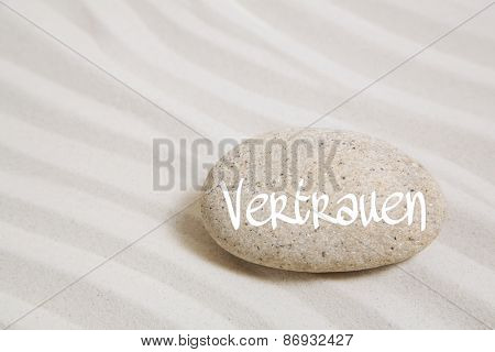 Sand background with a stone and the german word for trust.