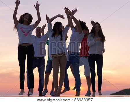 group of happy young people dancing and have fun on party in modern home bacony with sunset and ocean in background