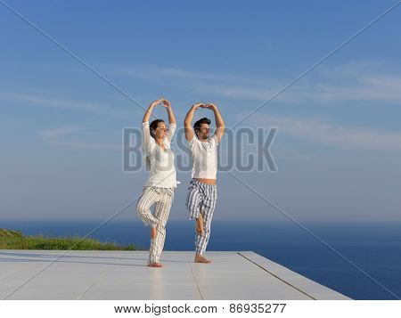 young couple practicing yoga at sunset in modern home terace with ocean and sunset in background