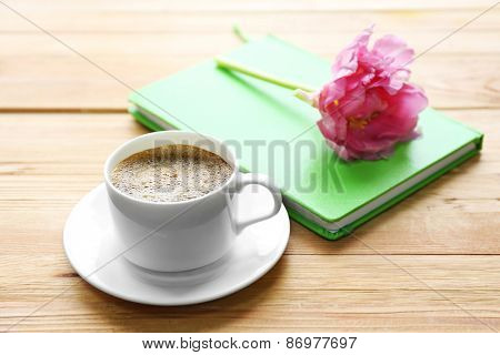 Cup of coffee with notebook and fresh flower on wooden table background