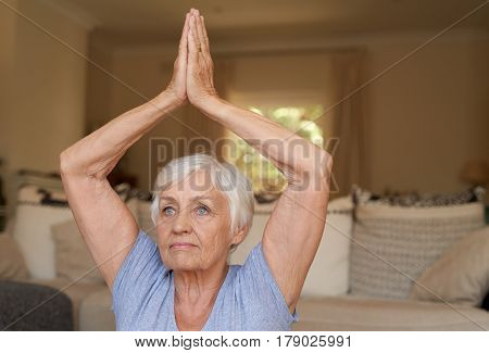 Active and focused senior woman doing the easy pose while practicing yoga alone in her living room at home