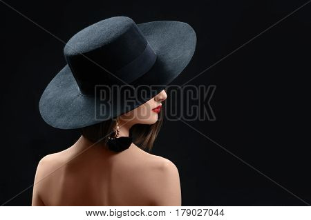 Rearview studio shot of a mysterious woman in a hat on black background red lips makeup cosmetics beauty fashion style elegance concept