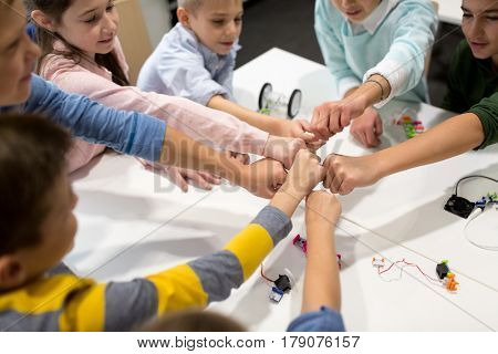 education, children, technology, science and people concept - group of happy kids with building kit making fist bump at robotics school