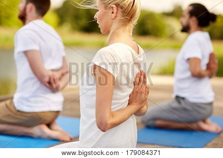 fitness, sport, yoga and healthy lifestyle concept - group of people exercising in reverse prayer pose on river or lake berth