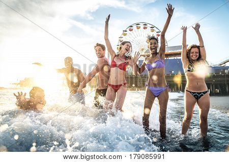 Group of friends splashing water while swimming in the sea - Multi-ethic group of people having fun on the beach