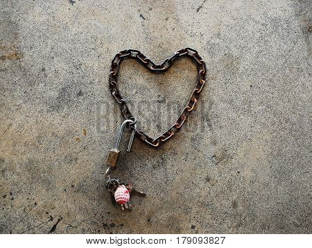 Detail old chain heart-shaped with brass padlock and many key on cememt floor for background