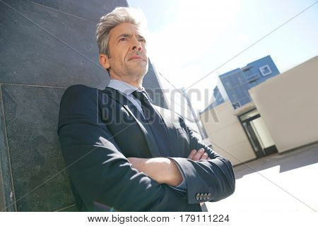 Portrait of businessman waiting outside building, leant on wall