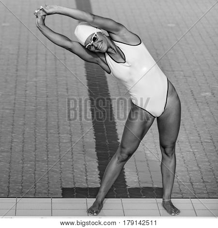 Female swimmer streching on poolside, black and white