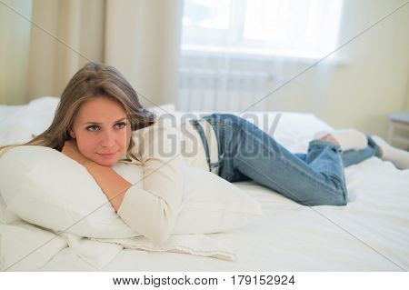 Smiling thoughtful pretty woman lying in bed at home.