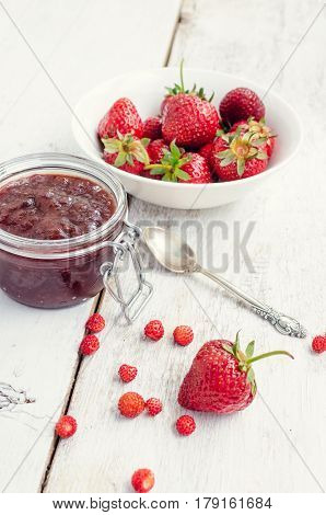 Homemade delicious strawberry jam in a glass jar and fresh strawberries on white rusric wooden background. Selective focus.