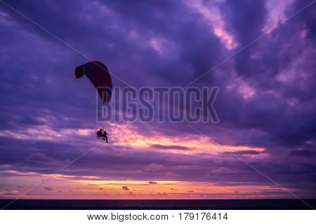 Paramotor glider flying in the sky over beautiful colorful clouds at sunset Bali Indoensia