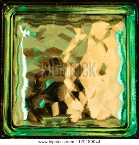 Green square glass block close up. Building material. Element of the wall. Refraction of light inside a glass object creates an interesting effect.