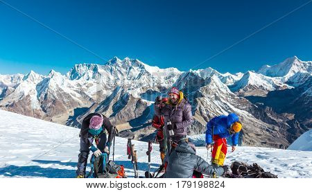 Group of Mountain Climbers in protective insulated Outwear alpine Gear and Ropes preparing for ascent on high Peak staying on snowcapped Glacier